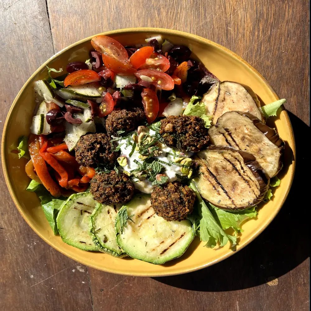 Bowl del Olimpo con falafel, berenjena y zucchini grillados, tomate, pepino y yogurt con hierbabuena, en un plato amarillo