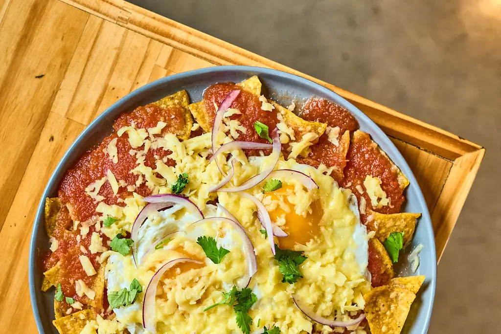 Chilaquiles vistos desde arriba en un plato gris: chips de maíz con salsa roja, huevo, queso rallado, cebolla morada y culantro
