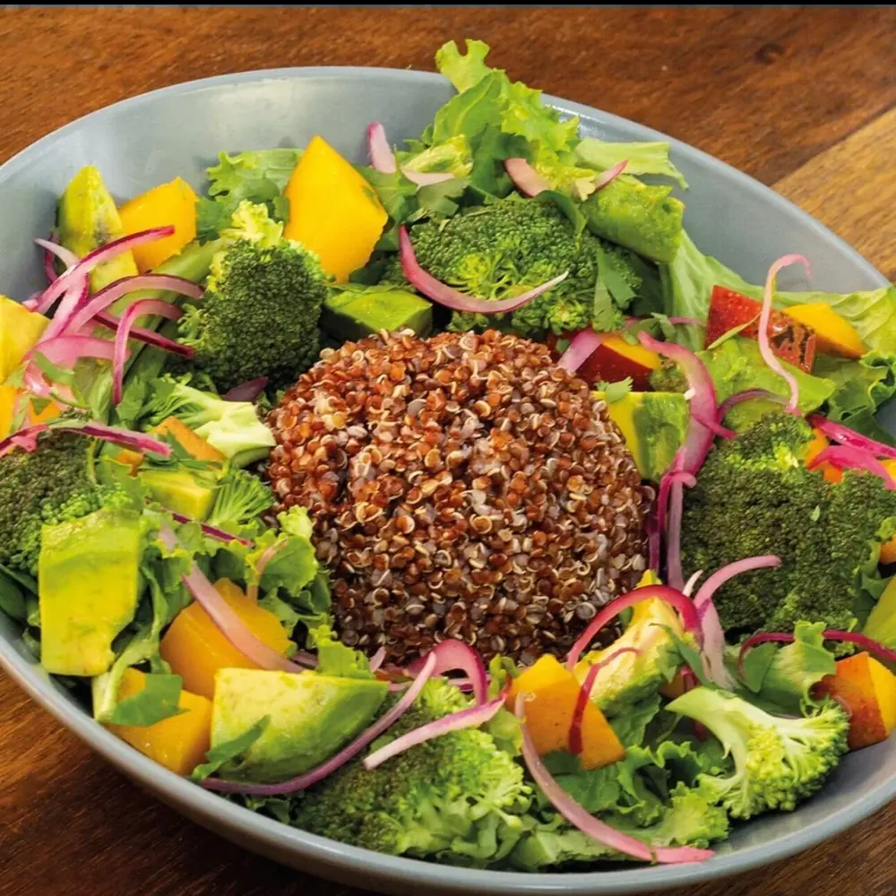 Ensalada Wö Kàpi con verdes, quinoa, manga, brócoli, aguacate y cebolla morada en un plato hondo